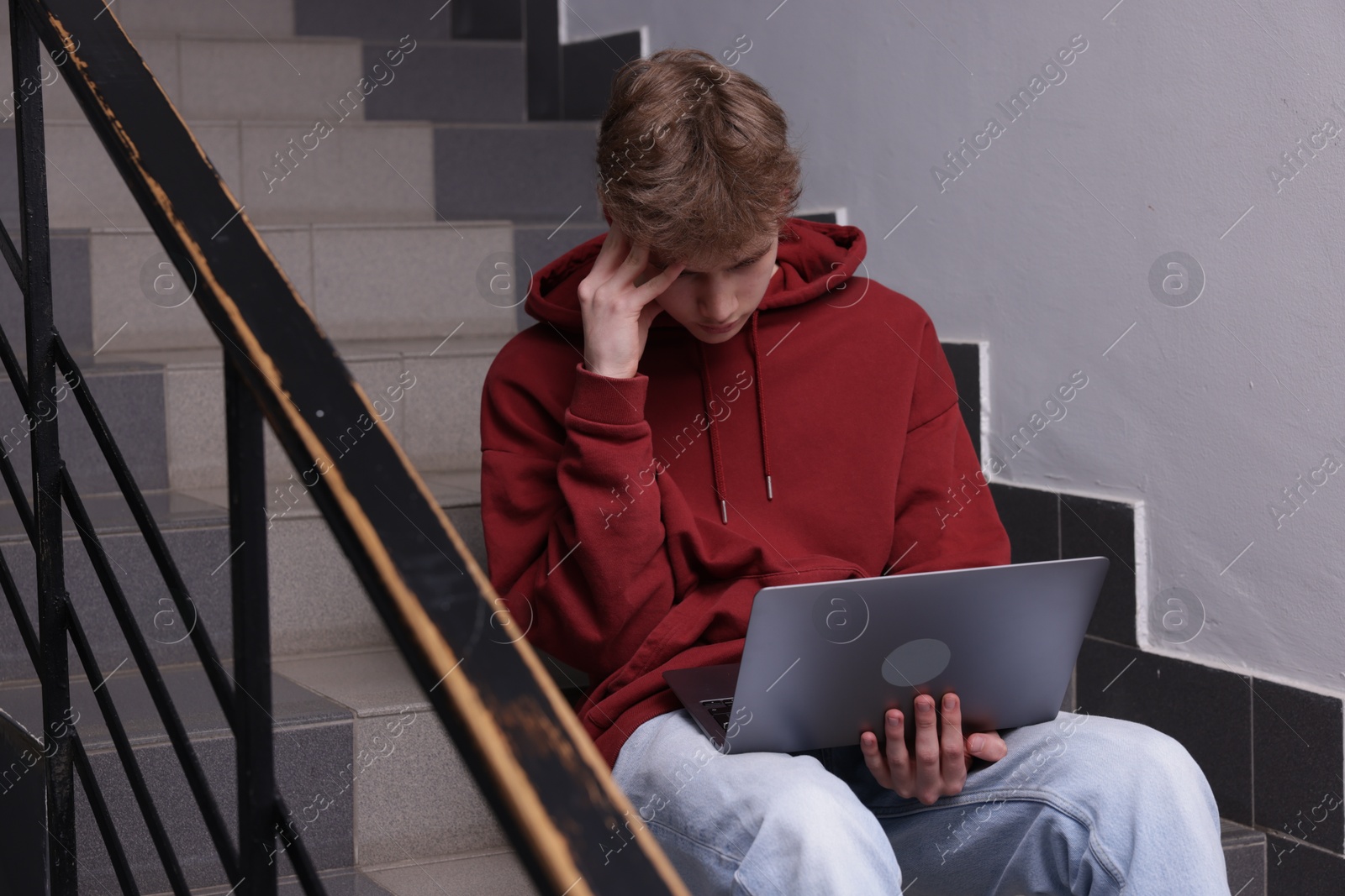 Cyber bullying. Upset teenage boy with laptop on stairs indoors Photo of Cyber bullying. Upset teenage boy with laptop on stairs indoors