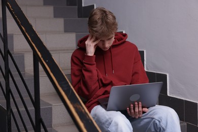 Photo of Cyber bullying. Upset teenage boy with laptop on stairs indoors