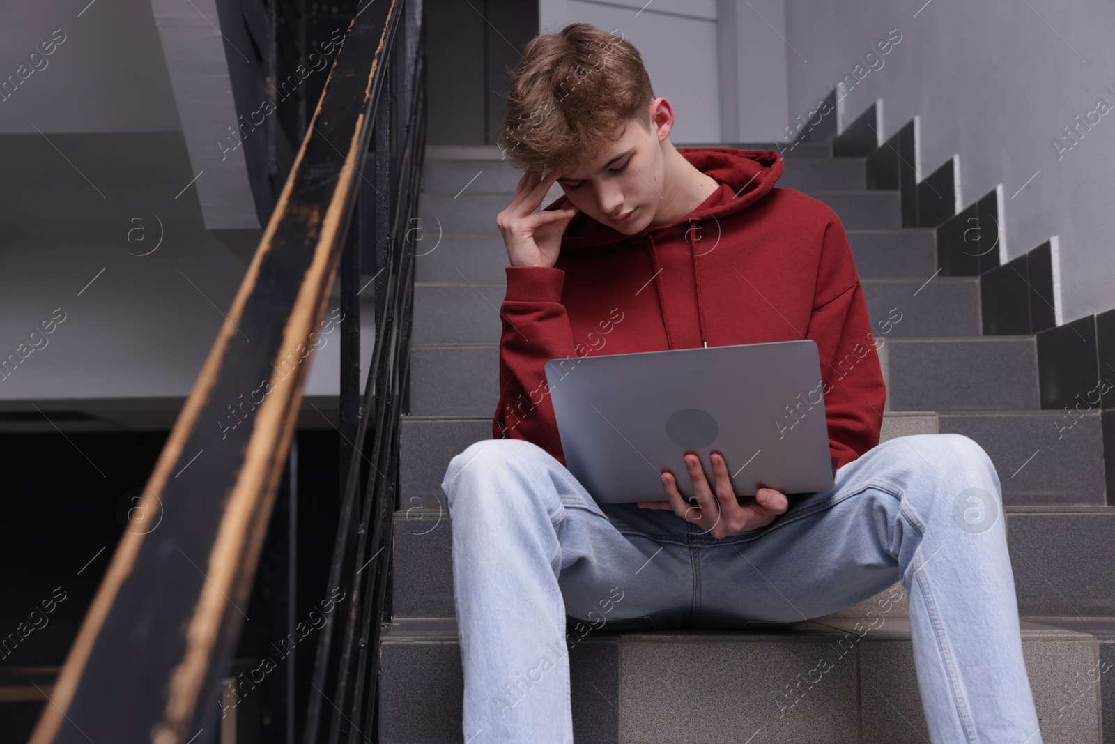 Cyber bullying. Upset teenage boy with laptop on stairs indoors Photo of Cyber bullying. Upset teenage boy with laptop on stairs indoors