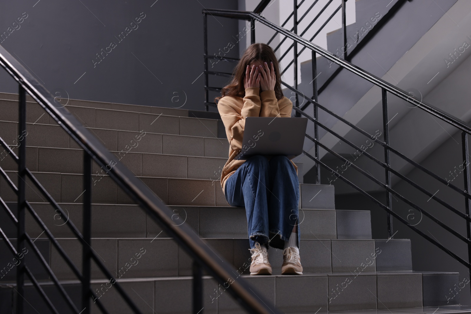 Cyber bullying. Upset teenage girl with laptop on stairs indoors Photo of Cyber bullying. Upset teenage girl with laptop on stairs indoors