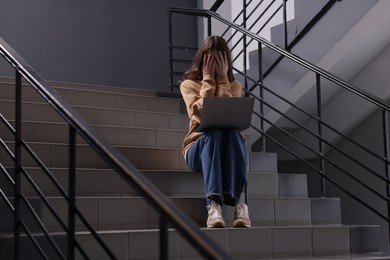 Photo of Cyber bullying. Upset teenage girl with laptop on stairs indoors