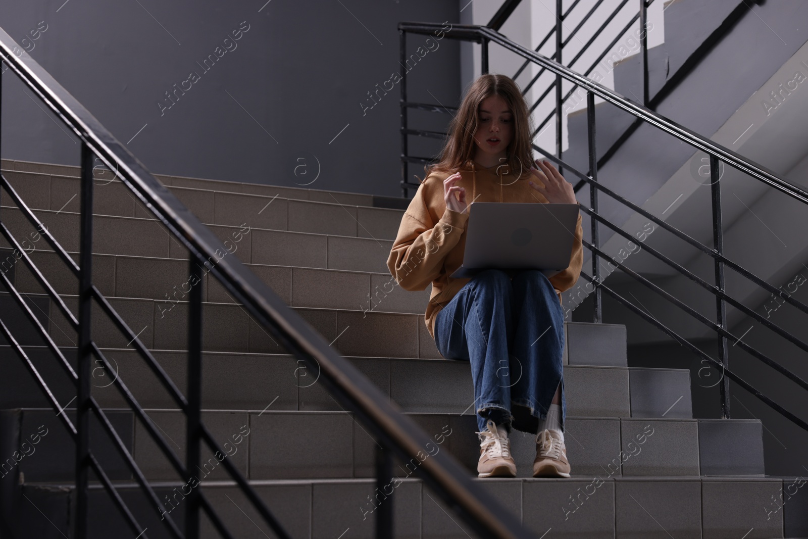 Cyber bullying. Upset teenage girl with laptop on stairs indoors. Space for text Photo of Cyber bullying. Upset teenage girl with laptop on stairs indoors. Space for text