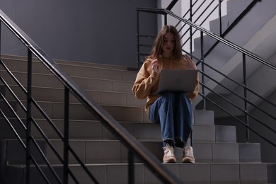 Photo of Cyber bullying. Upset teenage girl with laptop on stairs indoors. Space for text