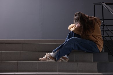 Photo of Bullying. Upset teenage girl on stairs indoors. Space for text