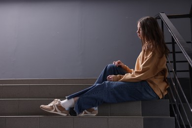 Photo of Bullying. Upset teenage girl on stairs indoors. Space for text