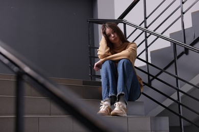Photo of Bullying. Upset teenage girl on stairs indoors