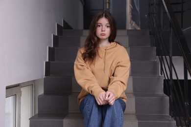 Photo of Bullying. Upset teenage girl on stairs indoors