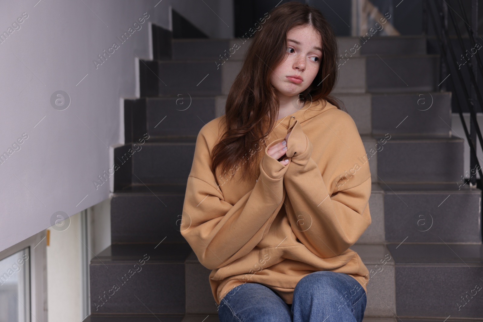 Photo of Bullying. Upset teenage girl on stairs indoors