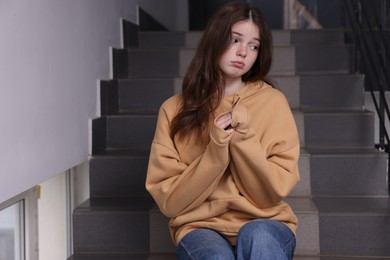 Photo of Bullying. Upset teenage girl on stairs indoors