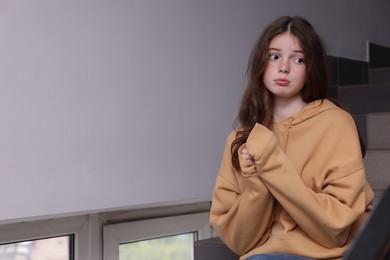 Photo of Bullying. Upset teenage girl on stairs indoors. Space for text