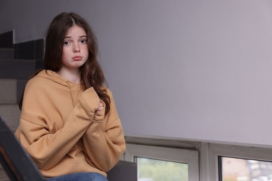 Photo of Bullying. Upset teenage girl on stairs indoors. Space for text