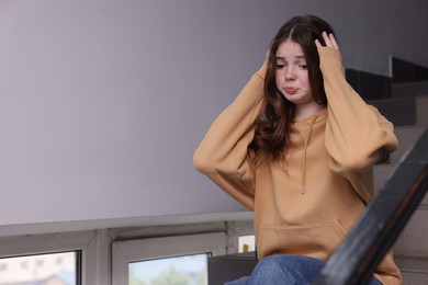 Photo of Bullying. Upset teenage girl on stairs indoors. Space for text