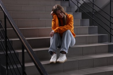 Photo of Bullying. Upset teenage girl on stairs indoors
