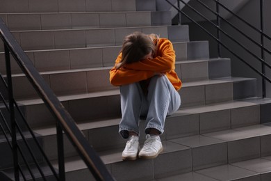 Photo of Bullying. Upset teenage girl on stairs indoors