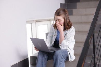 Photo of Cyber bullying. Upset teenage girl with laptop on stairs indoors
