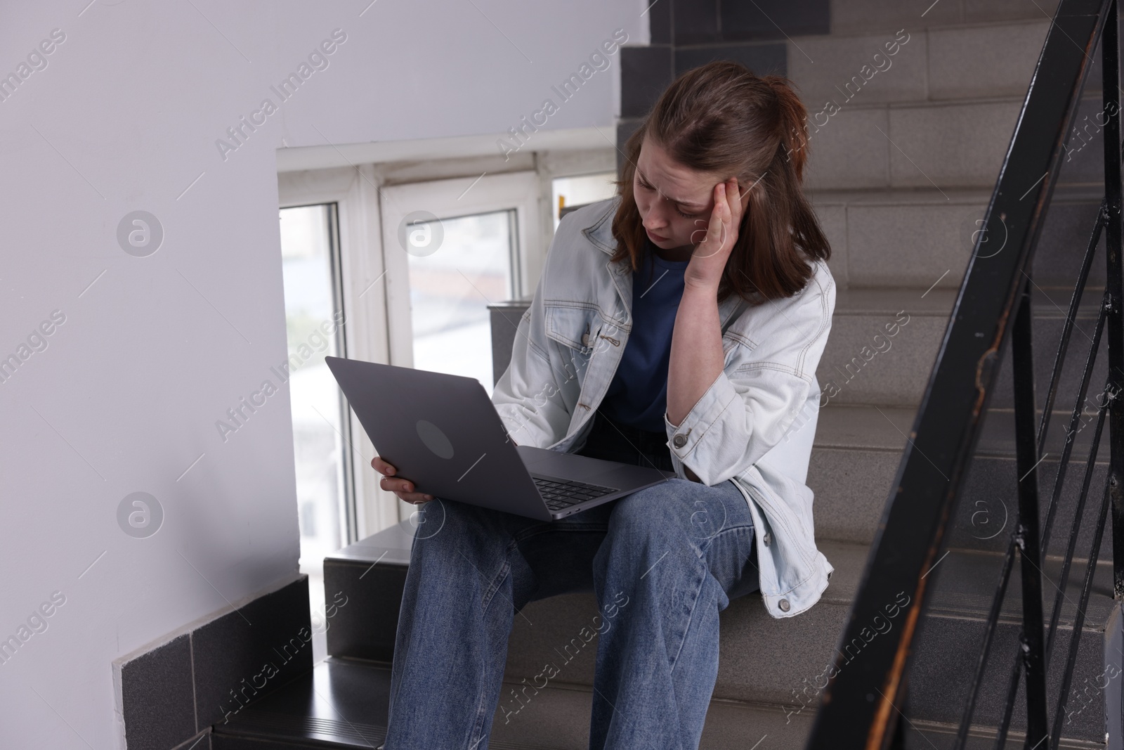 Cyber bullying. Upset teenage girl with laptop on stairs indoors Photo of Cyber bullying. Upset teenage girl with laptop on stairs indoors