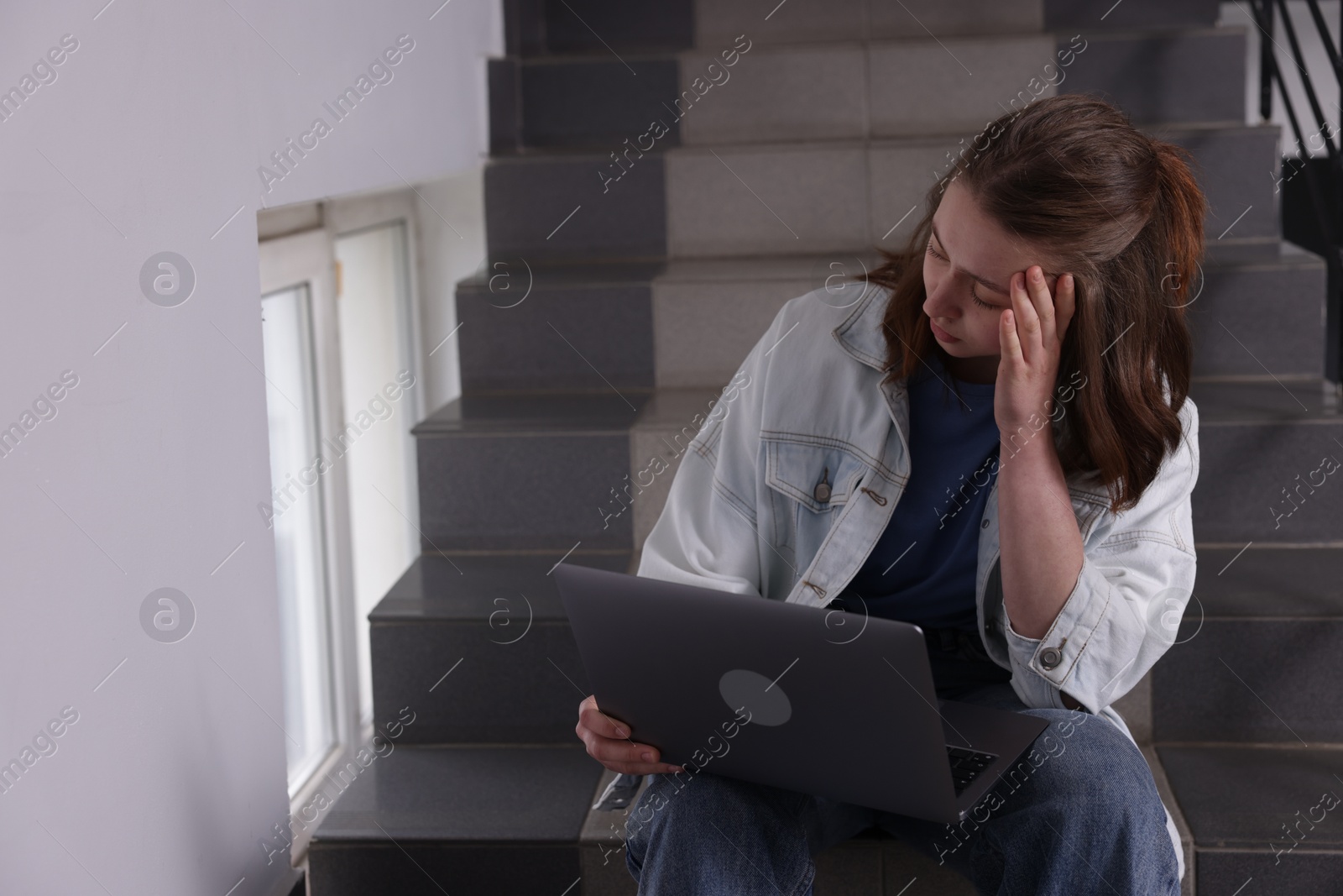 Cyber bullying. Upset teenage girl with laptop on stairs indoors. Space for text Photo of Cyber bullying. Upset teenage girl with laptop on stairs indoors. Space for text