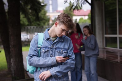 Photo of Teenage boy with smartphone suffering from bullying at school, selective focus