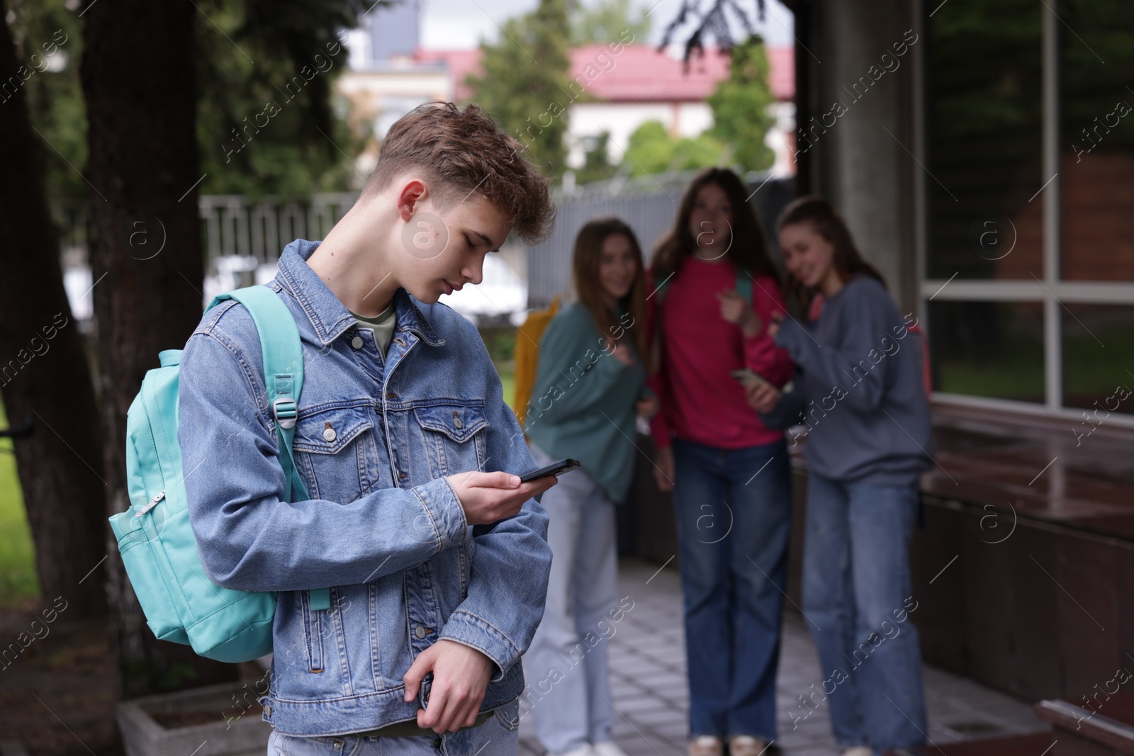 Teenage boy with smartphone suffering from bullying at school, selective focus Photo of Teenage boy with smartphone suffering from bullying at school, selective focus