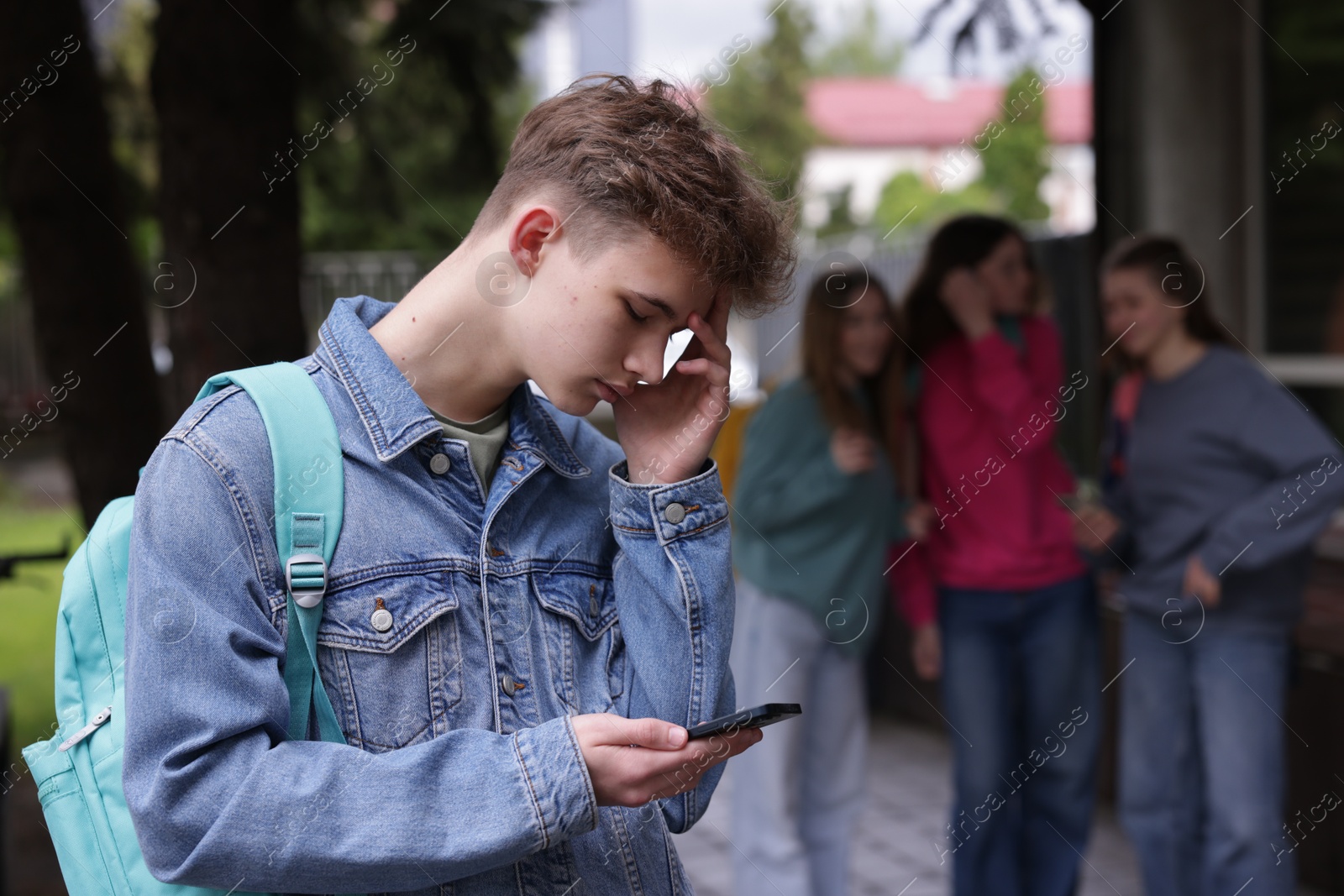 Teenage boy with smartphone suffering from bullying at school, selective focus Photo of Teenage boy with smartphone suffering from bullying at school, selective focus