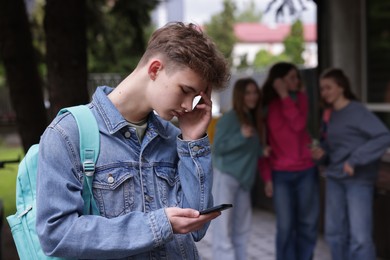Photo of Teenage boy with smartphone suffering from bullying at school, selective focus
