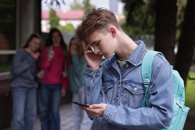 Photo of Teenage boy with smartphone suffering from bullying at school, selective focus