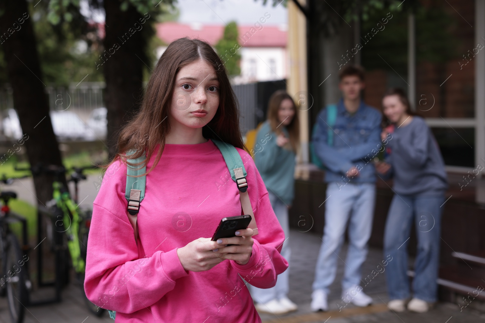 Teenage girl with smartphone suffering from bullying at school, selective focus Photo of Teenage girl with smartphone suffering from bullying at school, selective focus