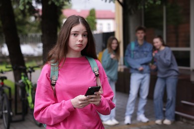 Photo of Teenage girl with smartphone suffering from bullying at school, selective focus
