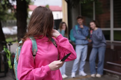 Photo of Teenage girl with smartphone suffering from bullying at school, selective focus