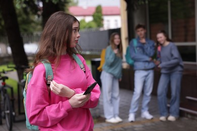 Photo of Teenage girl with smartphone suffering from bullying at school, selective focus