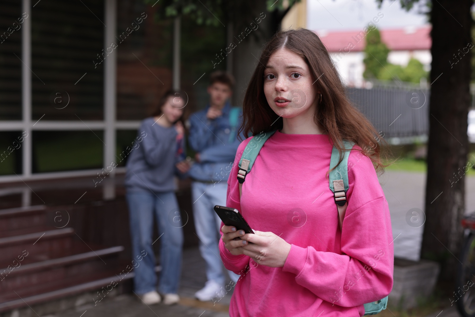Teenage girl with smartphone suffering from bullying at school, selective focus Photo of Teenage girl with smartphone suffering from bullying at school, selective focus