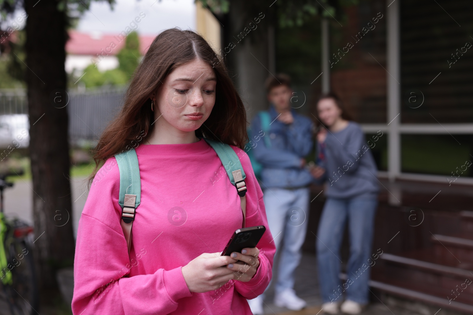 Teenage girl with smartphone suffering from bullying at school, selective focus Photo of Teenage girl with smartphone suffering from bullying at school, selective focus