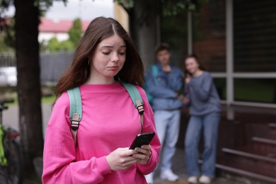 Photo of Teenage girl with smartphone suffering from bullying at school, selective focus