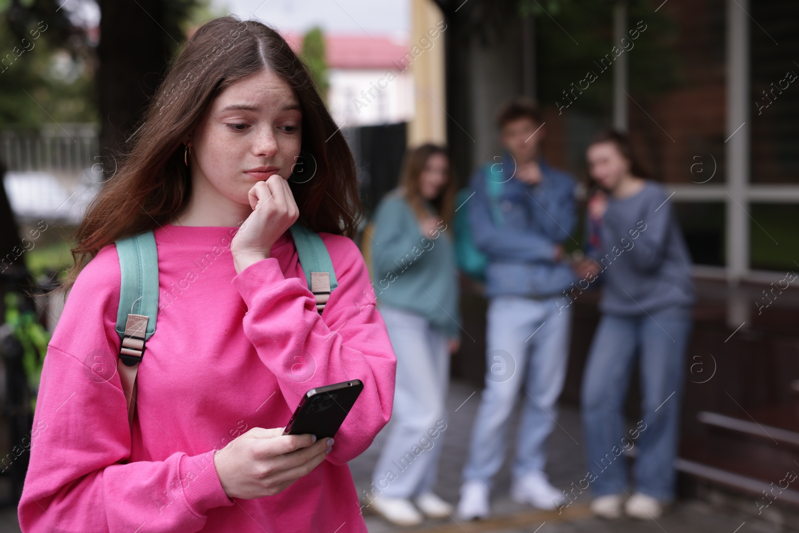 Teenage girl with smartphone suffering from bullying at school, selective focus Photo of Teenage girl with smartphone suffering from bullying at school, selective focus