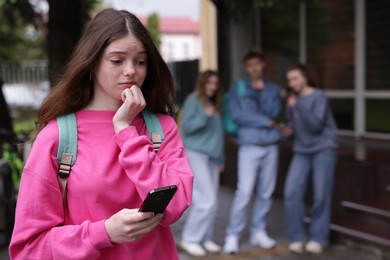 Photo of Teenage girl with smartphone suffering from bullying at school, selective focus