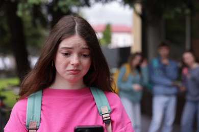 Photo of Teenage girl with smartphone suffering from bullying at school, selective focus