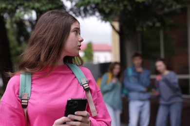 Photo of Teenage girl with smartphone suffering from bullying at school, selective focus