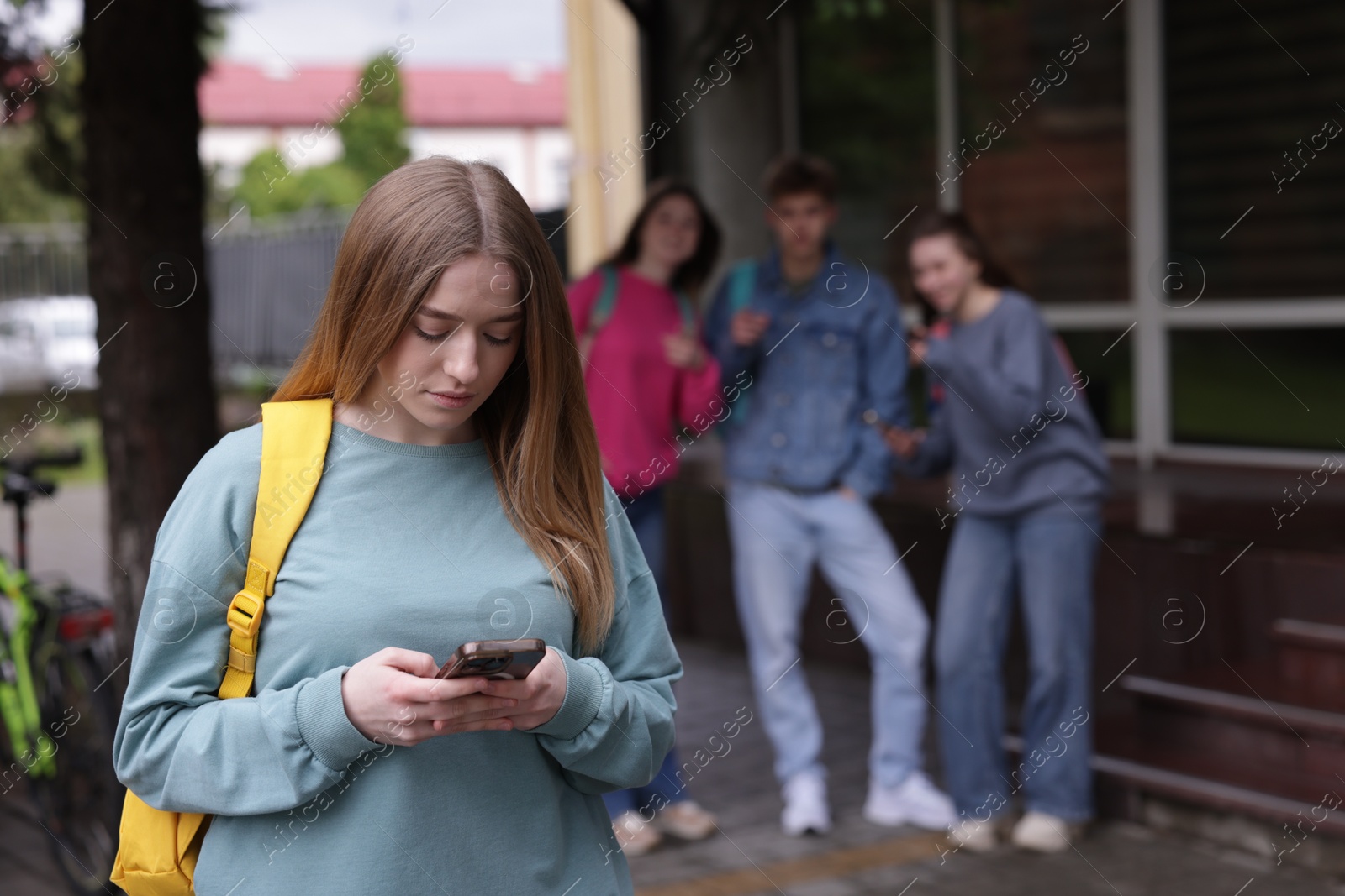 Teenage girl with smartphone suffering from bullying at school, selective focus Photo of Teenage girl with smartphone suffering from bullying at school, selective focus