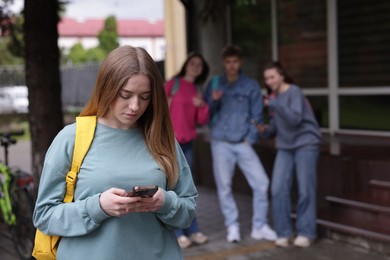 Photo of Teenage girl with smartphone suffering from bullying at school, selective focus