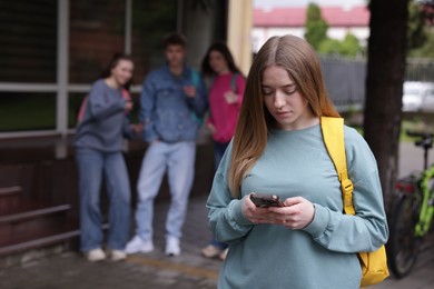 Photo of Teenage girl with smartphone suffering from bullying at school, selective focus