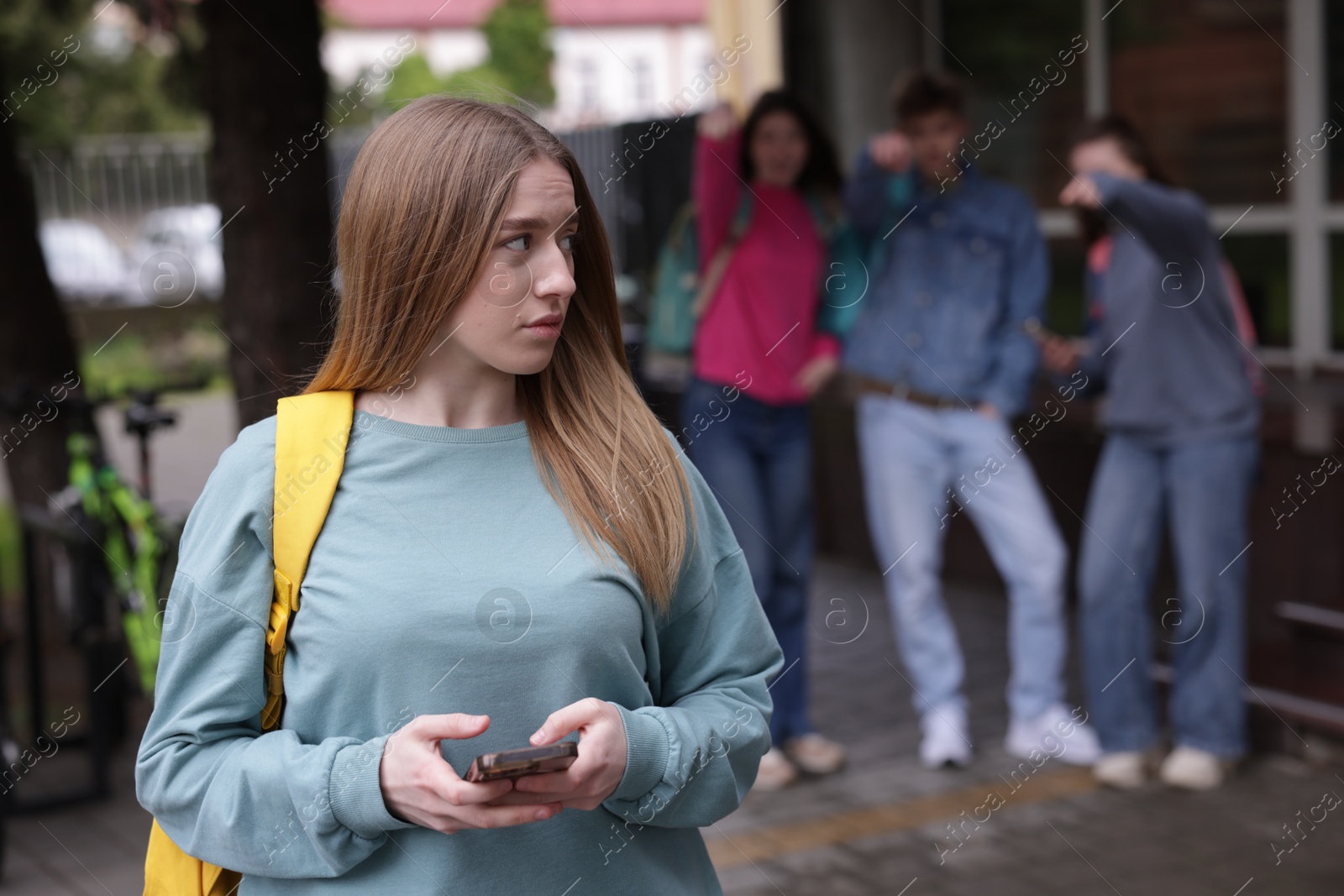 Teenage girl with smartphone suffering from bullying at school, selective focus Photo of Teenage girl with smartphone suffering from bullying at school, selective focus