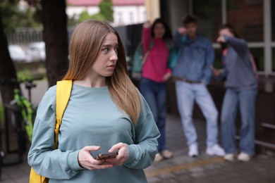 Photo of Teenage girl with smartphone suffering from bullying at school, selective focus