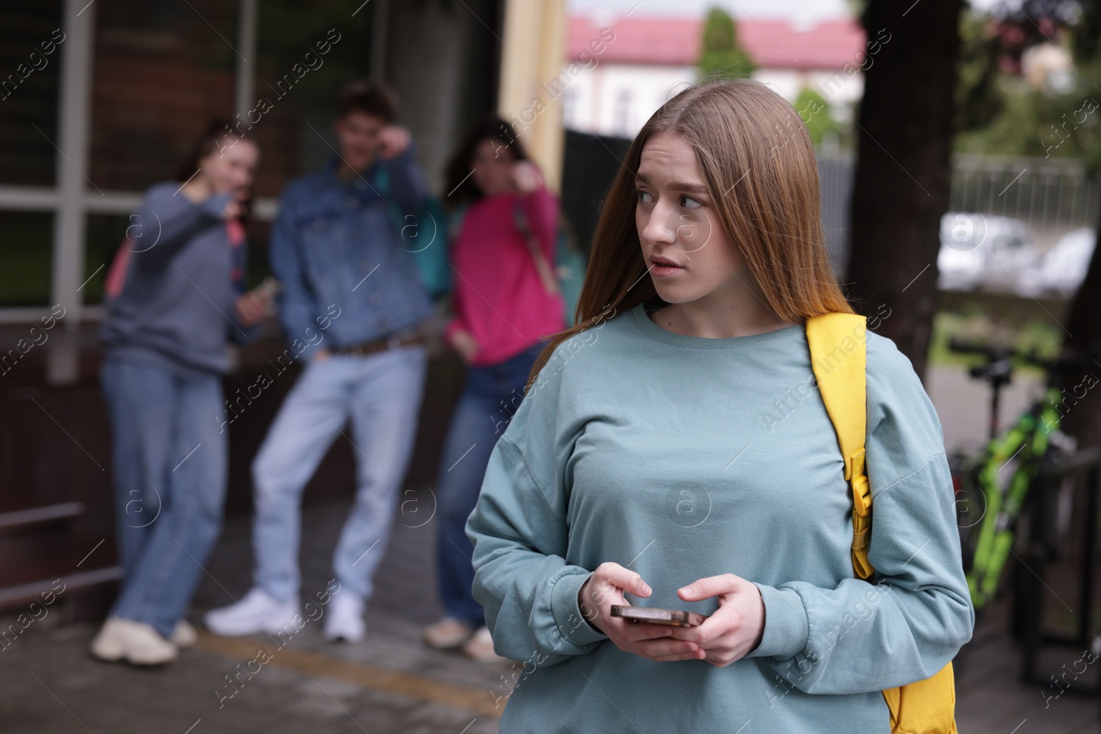 Teenage girl with smartphone suffering from bullying at school, selective focus Photo of Teenage girl with smartphone suffering from bullying at school, selective focus