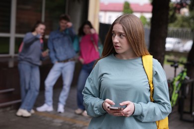 Photo of Teenage girl with smartphone suffering from bullying at school, selective focus