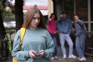 Photo of Teenage girl with smartphone suffering from bullying at school, selective focus