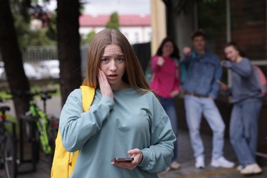 Photo of Teenage girl with smartphone suffering from bullying at school, selective focus