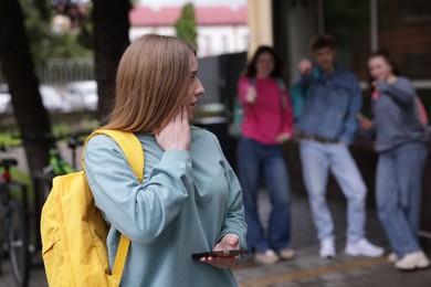 Photo of Teenage girl with smartphone suffering from bullying at school, selective focus