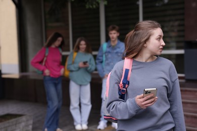 Photo of Teenage girl with smartphone suffering from bullying at school, selective focus