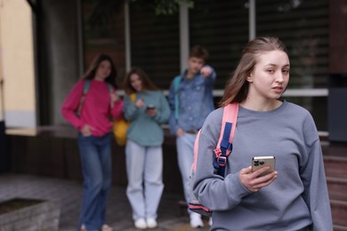 Photo of Teenage girl with smartphone suffering from bullying at school, selective focus