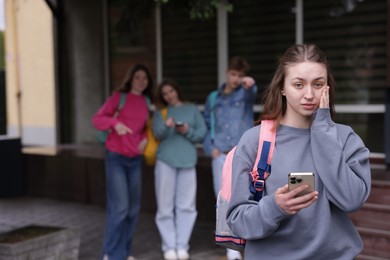 Photo of Teenage girl with smartphone suffering from bullying at school, selective focus